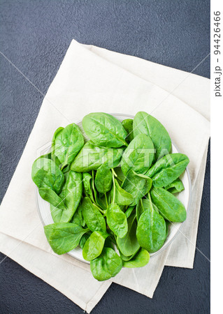 Fresh baby spinach leaves in drops of water on a plate on a black background. Vegetarian, wellness and detox food. Top and vertical view 94426466
