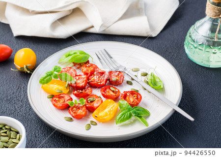 Diet vegetarian snack. Sun-dried tomatoes with basil, sesame seeds and pumpkin on a plate on a black background 94426550