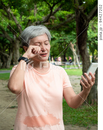 Portrait of senior adult elderly asian woman 60s smiling standing and having eyestrain using smartphone in the park. Portrait of senior adult elderly asian woman 60s smiling standing and having eyestrain using smartphone in the park. 94427202