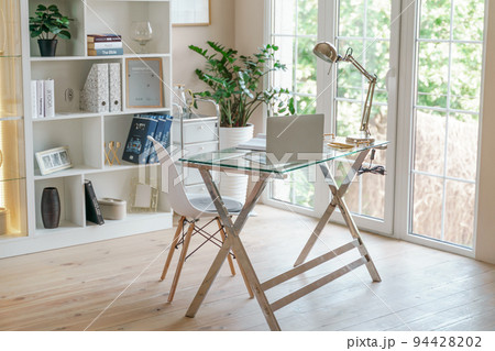 Comfortable workplace with a laptop in the office, at home. Bright room with large windows, bookcase, green plant. Remote work, freelance. 94428202