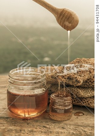 Delicious honey dripping from Wooden honey dipper stick into on Fresh honeycombs. Healthy organic natura honey, space for text, 94431708