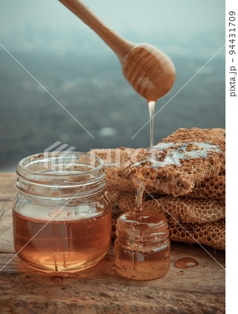 Delicious honey dripping from Wooden honey dipper stick into on Fresh honeycombs. Healthy organic natura honey, space for text, 94431709