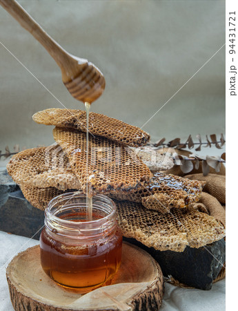 Delicious honey dripping from Wooden honey dipper stick into on Glass jar and Fresh honeycombs background. 94431721