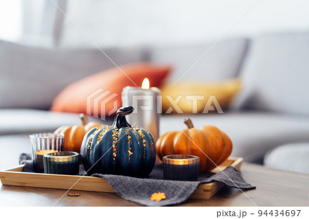 Autumn cozy mood composition for hygge home decor. Orange and gray pumpkins , burning candles on the tray with gray napkin on the coffee table in the living room. Selective focus. Copy space. Autumn cozy mood composition for hygge home decor. Orange and gray pumpkins , burning candles on the tray with gray napkin on the coffee table in the living room. Selective focus. Copy space. 94434697