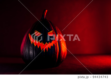 Spooky halloween black pumpkin, Jack O Lantern, with illuminated evil face and eyes on bloody red and black background with copy space. Happy Halloween decor concept. Festive postcard. Selective focus 94434743
