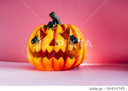 Bright pink Halloween background with carved orange pumpkin. Halloween Jack-o-lantern with spiders on it. Happy Halloween decor concept. Festive postcard with copy space. Selective focus 94434745