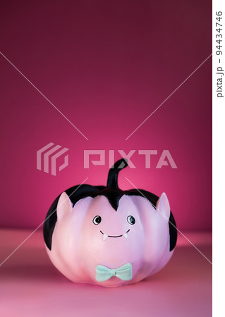 Halloween decorations on dark pink background. Funny and cute pink Vampire pumpkin with blue butterfly tie. Halloween vertical card. Concept of entertainer, emcee for festive fall, autumn events. 94434746