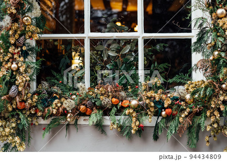 Winter holiday window decorated with fresh greens, red berries, cones and flowers. Outdoor exterior decoration made of natural materials. Christmas festive city. Selective focus. 94434809