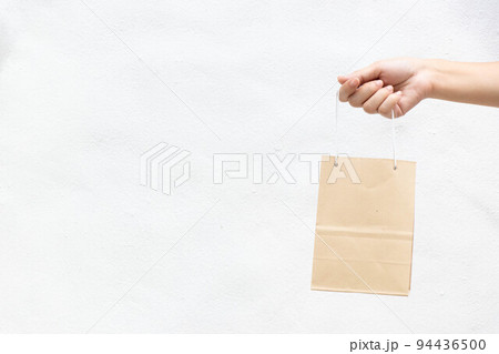 Hand of business woman hold brown paper shopping bag on white concrete background 94436500