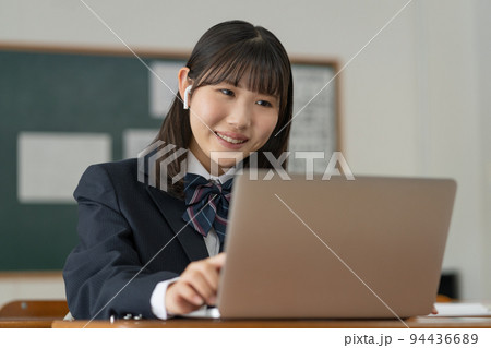 学校の教室でノートパソコンを使って勉強する女子高生 94436689