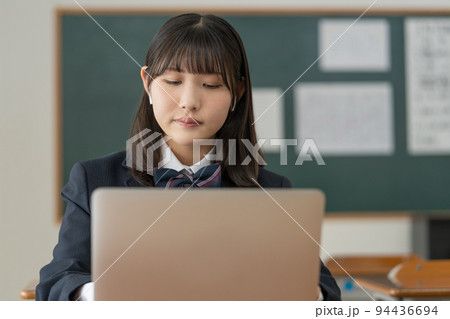 学校の教室でノートパソコンを使って勉強する女子高生 94436694