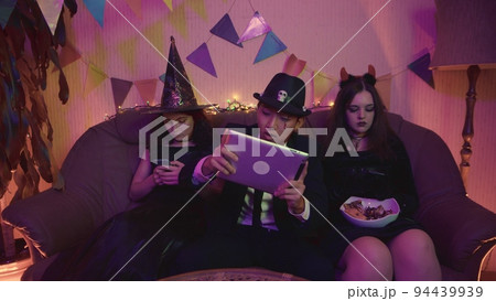 A guy in a creepy costume is actively playing on a tablet, and the girls are sitting on the phone at a Halloween party. A guy in a creepy costume is actively playing on a tablet, and the girls are sitting on the phone at a Halloween party. 94439939