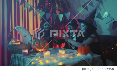 A group of friends celebrate Halloween and drink juice at the table from glasses in the form of a pumpkin A group of friends celebrate Halloween and drink juice at the table from glasses in the form of a pumpkin 94439950