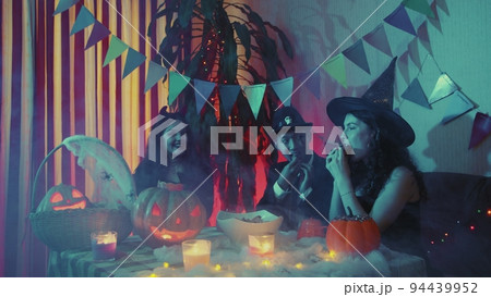 The guy pours candy into a plate. Friends celebrate Halloween by laughing and chatting together The guy pours candy into a plate. Friends celebrate Halloween by laughing and chatting together 94439952