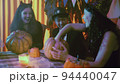 Two girls and a guy in creepy Halloween costumes are sitting at a table and taking the pulp out of pumpkins 94440047