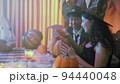 A girl and a guy in creepy Halloween costumes were sitting at a table and taking the pulp on pumpkins 94440048
