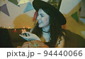 Close-up of a girl in a creepy Halloween costume sitting at a table, laughing and carving a face on a pumpkin 94440066
