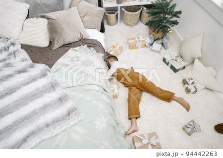 Little boy with Christmas gifts lying down on the floor 94442263