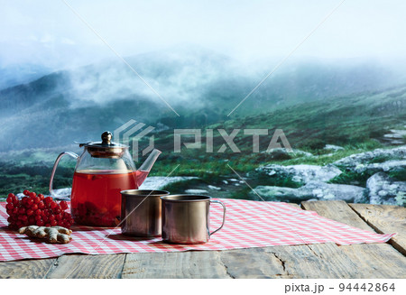 Glass pot with fruit or berries tea, cakes, biscuits on table over winter snow natural landscape background. Design for greeting card, poster for ad 94442864
