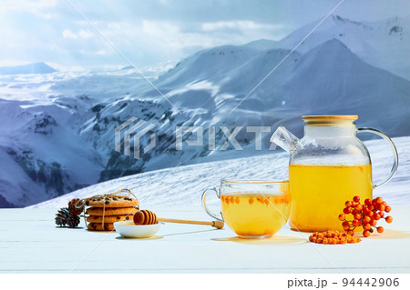 Tea with honey. Glass pot with fruit or berries tea, cakes, biscuits on table over winter snow natural landscape background. Design for greeting card 94442906
