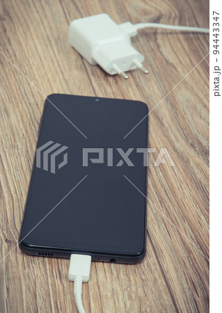 Black smartphone with charger. Various devices charging concept Black smartphone with charger. Various devices charging concept 94443347