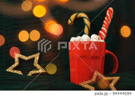 Red mug with hot cocoa and marshmallows on green background. Cozy Christmas home interior. Chocolate with licorice candies. Happy holidays, Merry Xmas, 2023 New Year concept 94444094