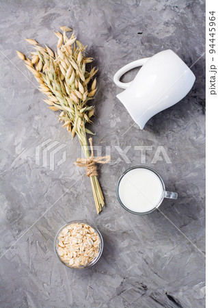 Oat milk in a cup, oatmeal and ears on a gray background. Alternative to cow's milk. Healthy eating. Top and vertical view Oat milk in a cup, oatmeal and ears on a gray background. Alternative to cow's milk. Healthy eating. Top and vertical view 94445964