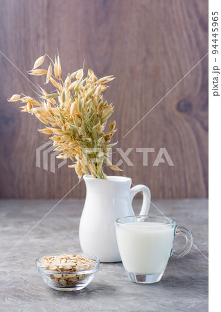 Oat milk in a cup, oatmeal and ears of corn in a jug on the table. Alternative to cow's milk. Healthy dietary non-allergenic food. Vertical view Oat milk in a cup, oatmeal and ears of corn in a jug on the table. Alternative to cow's milk. Healthy dietary non-allergenic food. Vertical view 94445965