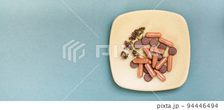 Herbal medicinal capsules, pills and dried oregano on a saucer on a green background. Alternative medicine. Copy space. Web banner Herbal medicinal capsules, pills and dried oregano on a saucer on a green background. Alternative medicine. Copy space. Web banner 94446494