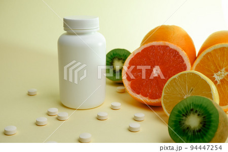 Vitamins. Medical concept. Pharmacy or natural. White bottle with vitamins, scattered pills. Juicy ripe citrus fruit slices. lemon. Orange. Grapefruit. Kiwi. 94447254