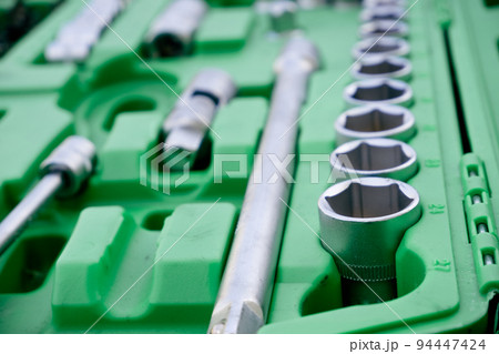 Chrome mechanics tools set. Close-up photo of a set of sockets with a screwdriver and a ratchet in a green plastic case against a background of green grass. Auto tool. 94447424