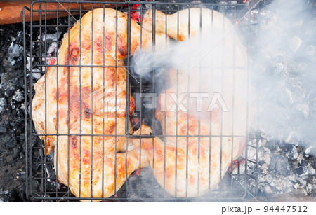 Cooking chicken meat over charcoal. Chicken meat fried with a crust on a wire rack during grill cooking. 94447512