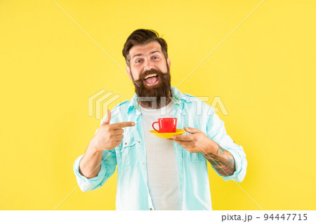happy unshaven man in shirt point finger on coffee on yellow backdrop, coffee 94447715