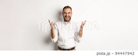 Frustrated and angry man screaming in rage, shaking hands furious, standing over white background 94447942