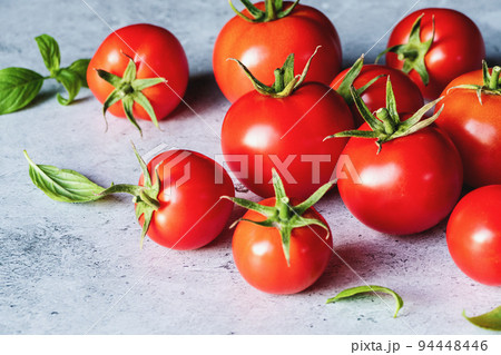 Red tomatoes with green basil leaves on gray concrete background, selective focus Red tomatoes with green basil leaves on gray concrete background, selective focus 94448446
