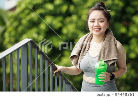 Smiling fit young woman walking up stairs with protein shake in hand after working out outdoors Smiling fit young woman walking up stairs with protein shake in hand after working out outdoors 94448861