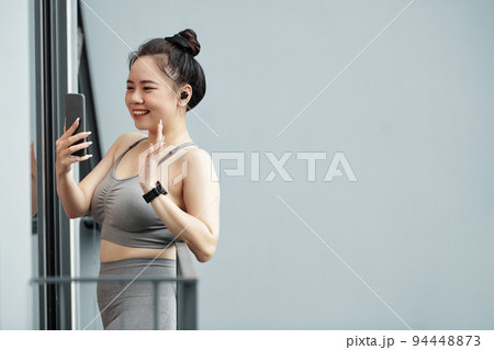 Smiling young Asian woman standing on apartment balcony and video calling her friend 94448873