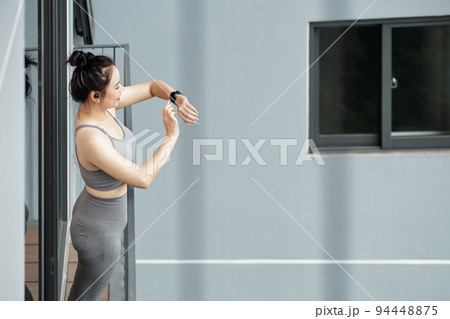 Young woman standing on balcony and checking fitness tracker after working out at home Young woman standing on balcony and checking fitness tracker after working out at home 94448875