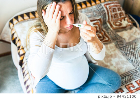 Pregnancy fever temperature check. Pregnant woman holding thermometer, check fever flu temperature. Pregnancy girl sick. Concept maternity, pregnant, childbirth. 94451100