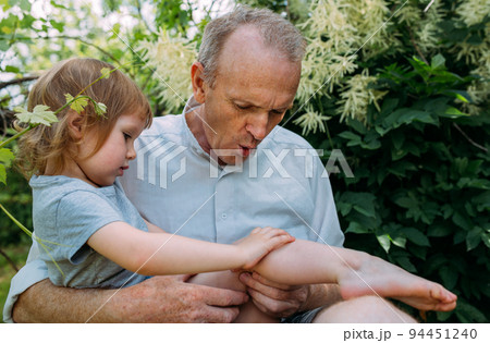A little girl hugs her grandfather on a walk in the summer outdoors.  94451240