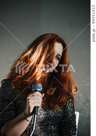 Portrait of redhead female singer woman in sparkly evening dress holding microphone. Singer at microphone. Woman singing and holding mic. Female vocal talent. Music show recital. 94451415