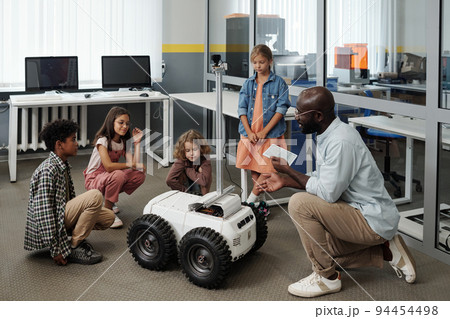 Young teacher of robotics with tablet making presentation of crawler to kids 94454498