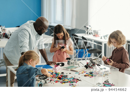 Group of youthful learners constructing robots at lesson with teacher advice 94454662