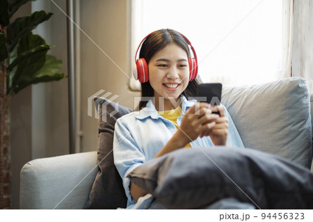 Young asian woman smiling listening to music using smartphone at home. Young asian woman smiling listening to music using smartphone at home. 94456323