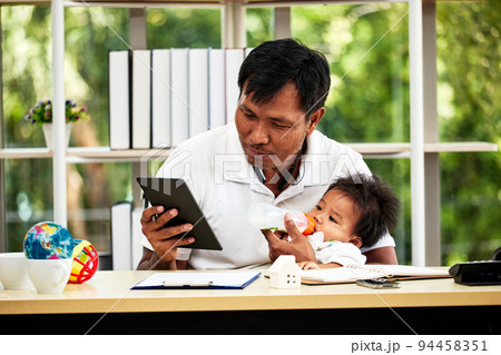 Young father working from home and holding his baby boy feeding milk and digital tablet Young father working from home and holding his baby boy feeding milk and digital tablet 94458351