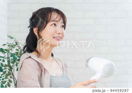 部屋でドライヤーを使ってヘアブローする女性 94459297