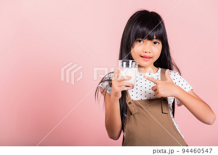 Asian little kid 10 years old smile hold milk glass drink white milk and pointing finger Asian little kid 10 years old smile hold milk glass drink white milk and pointing finger 94460547