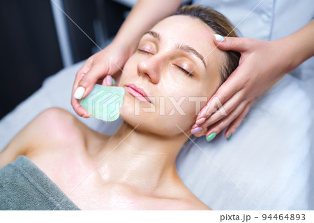 Woman having an gua sha facial massage with natural jade stone massager in the salon Woman having an gua sha facial massage with natural jade stone massager in the salon 94464893