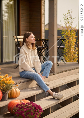 Pensive young woman seated on the veranda of her cottage Pensive young woman seated on the veranda of her cottage 94466012