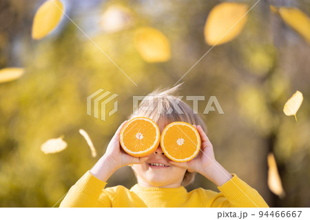 Surprised child holding slices of orange in autumn park 94466667